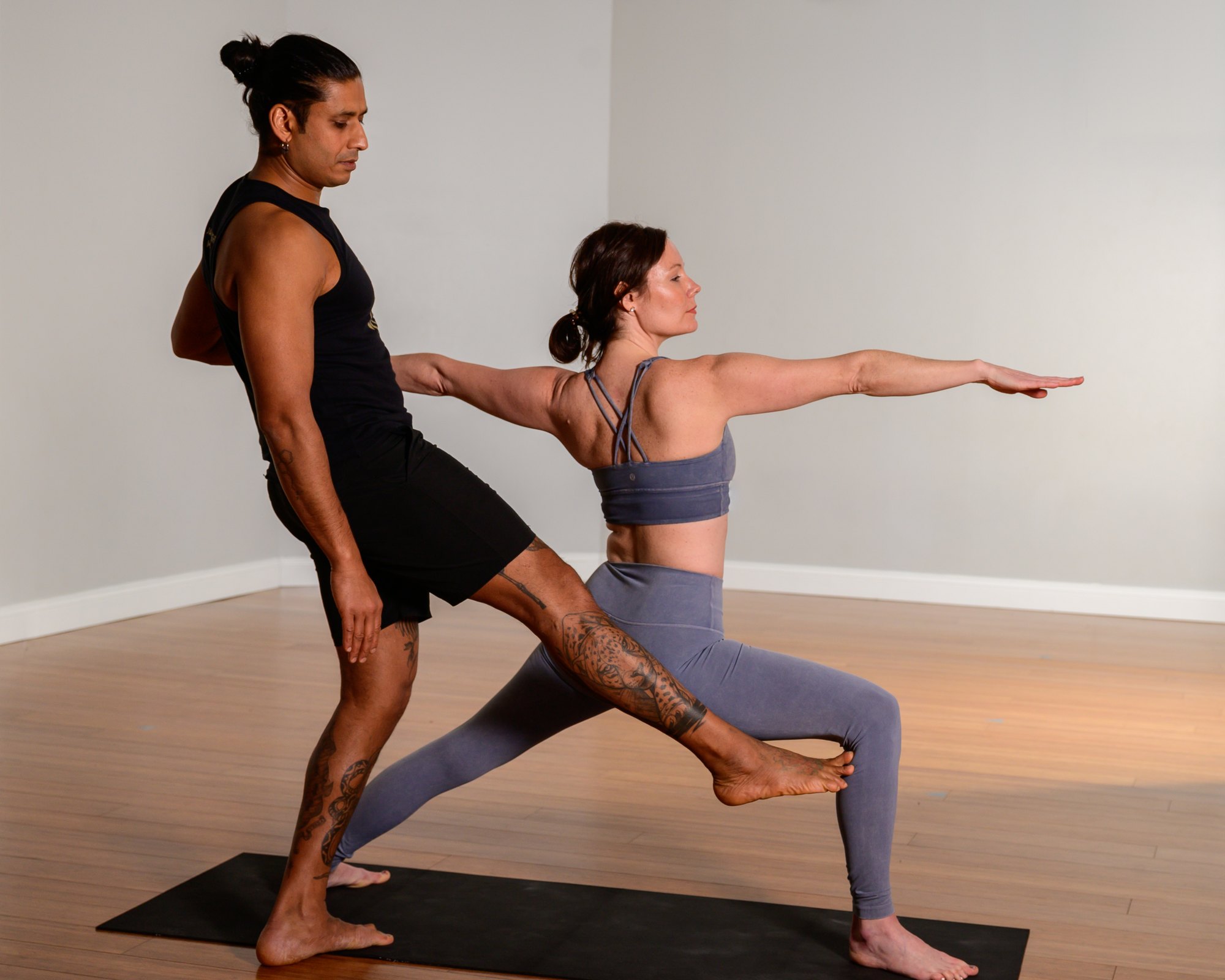 Jai guiding a student in a warrior pose on a yoga mat